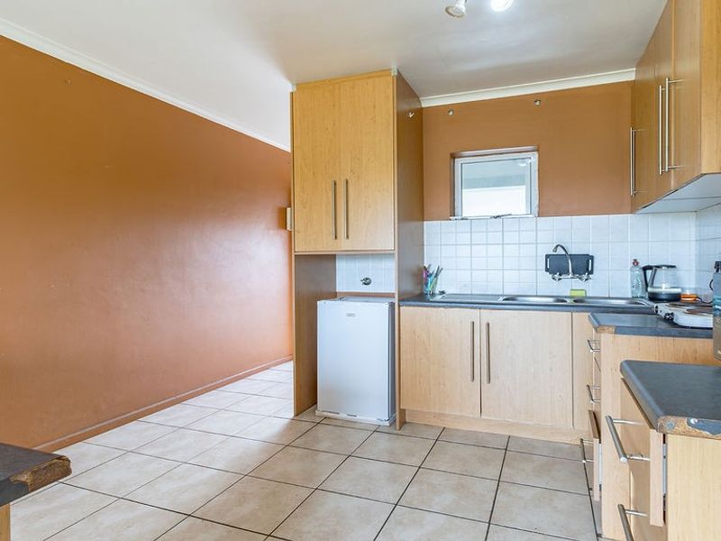A functional kitchen featuring light wood-finish cabinetry, tiled backsplash, and durable ceramic floor tiles, offering a practical layout for daily use.