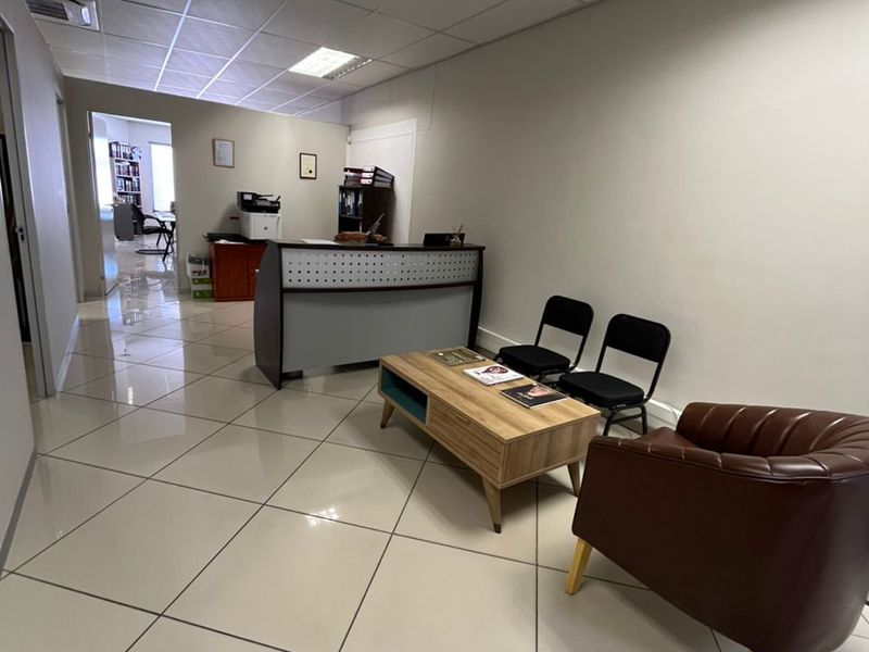 A professional office reception area featuring polished tiled flooring, a suspended ceiling with recessed lighting, and a built-in reception desk.