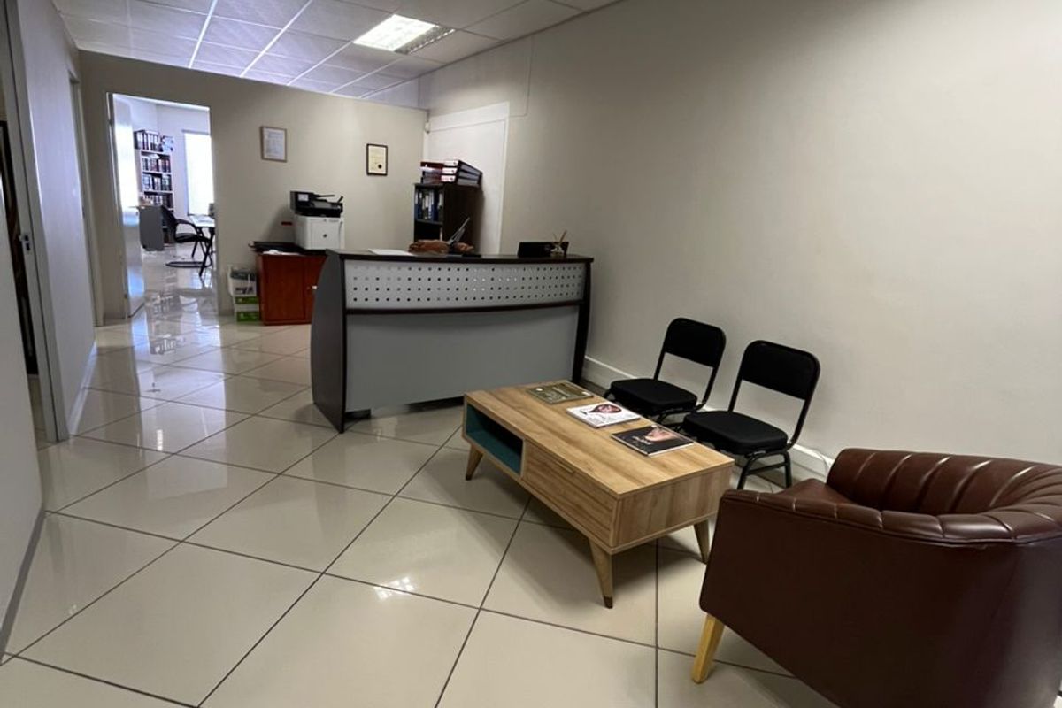 A professional office reception area featuring polished tiled flooring, a suspended ceiling with recessed lighting, and a built-in reception desk.