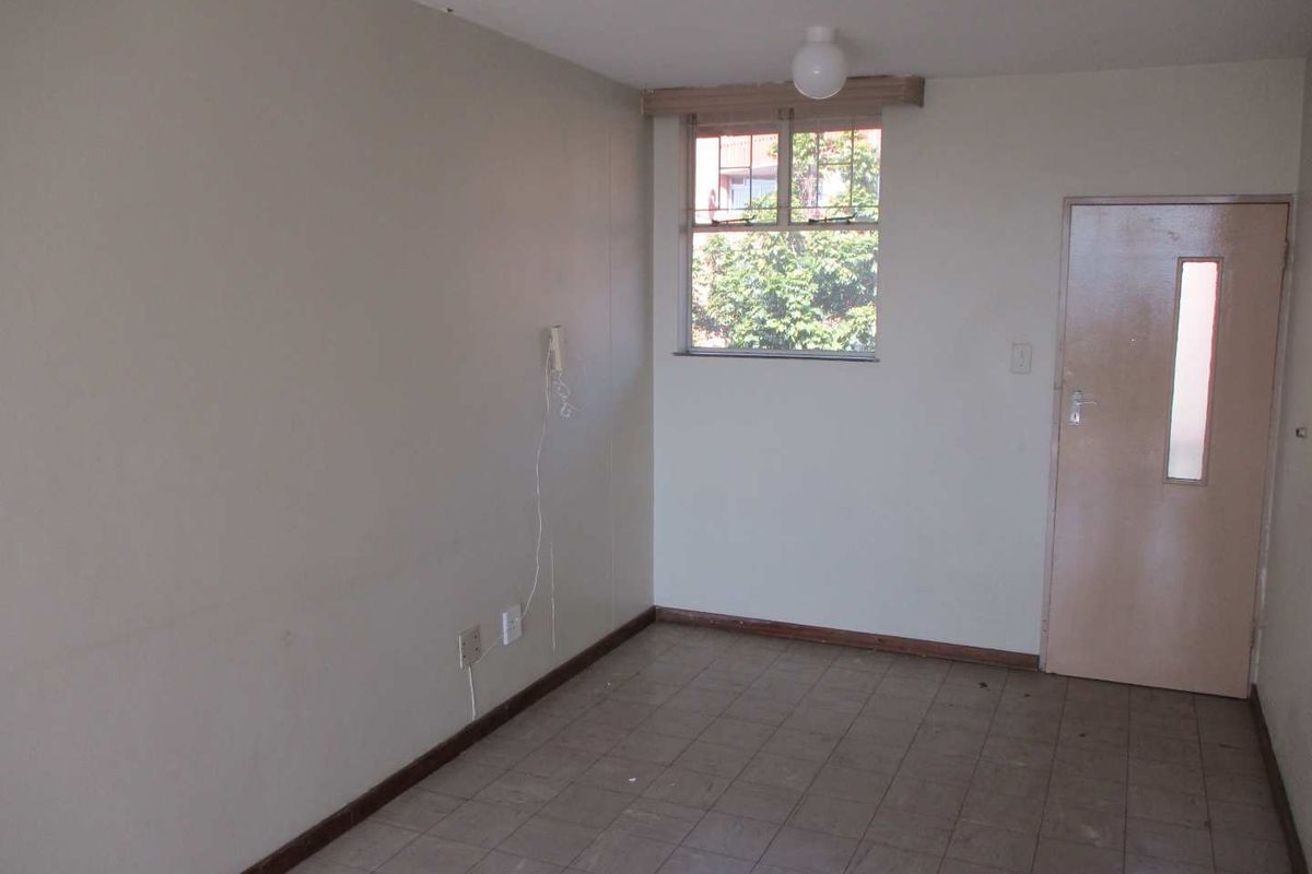 An empty, neutrally painted bedroom featuring tiled flooring, a single-pane window, and a standard internal door, ready for renovation or staging.