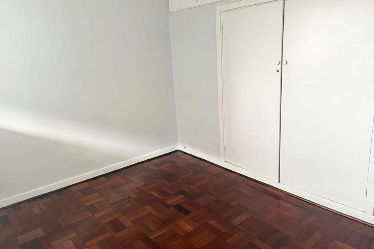 A clean, empty bedroom featuring classic parquet timber flooring and ample built-in cupboard storage with overhead cabinets.