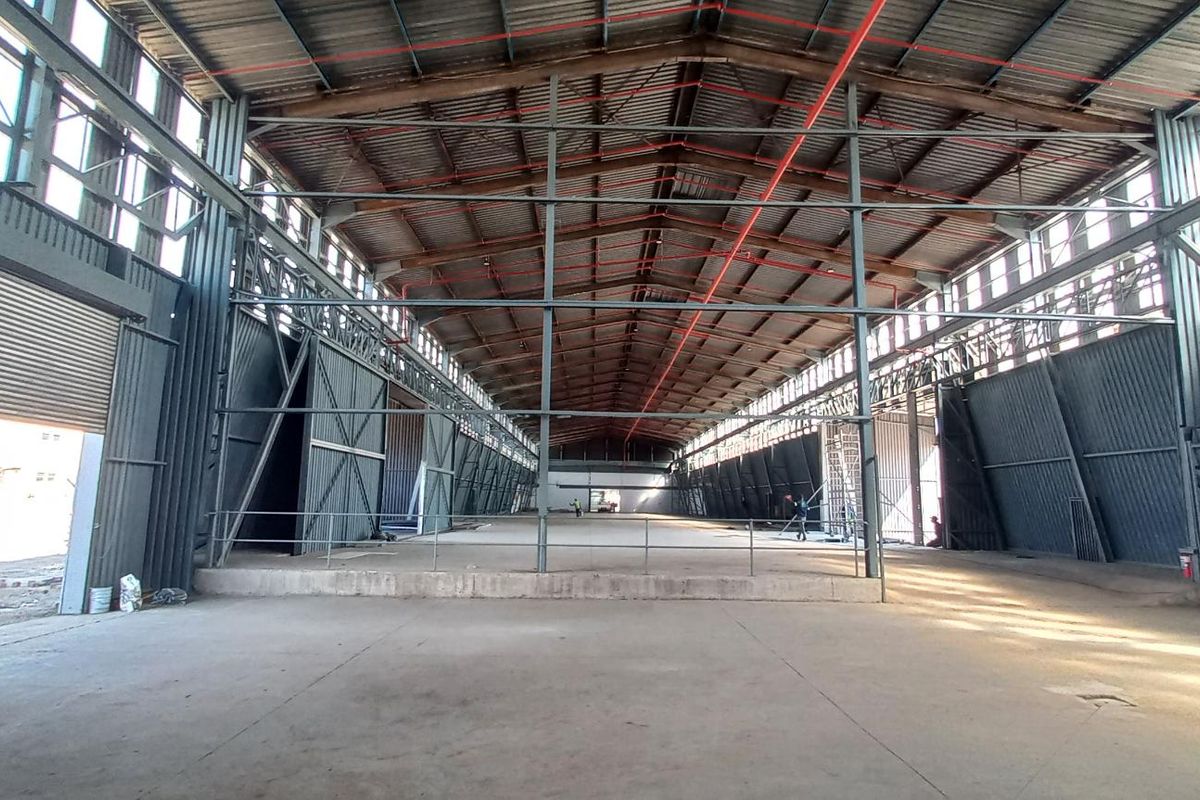 Spacious industrial warehouse featuring a high-clearance steel portal frame, concrete flooring, fire sprinkler system, and large roller shutter access.