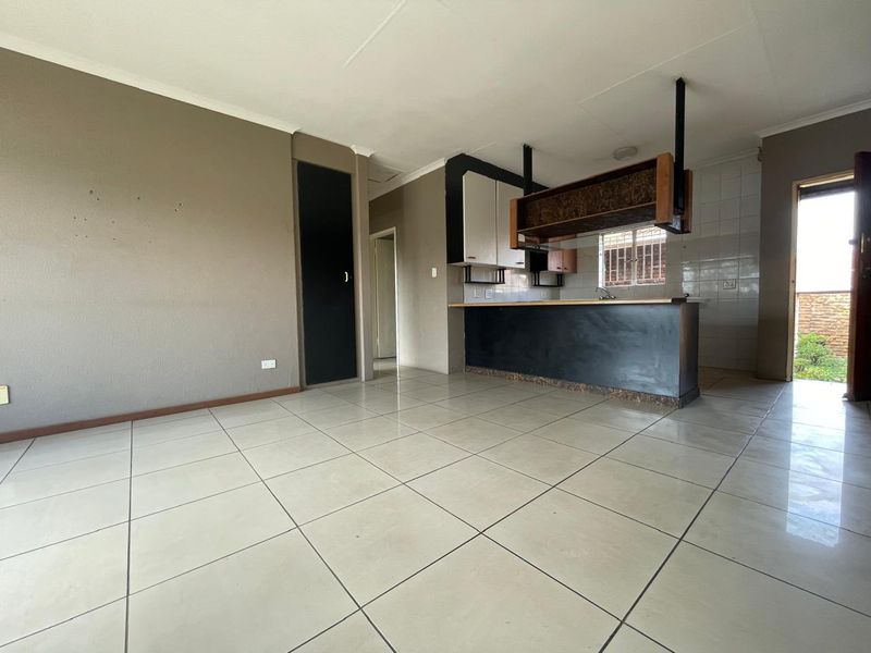 Open-plan living and kitchen area featuring tiled flooring, a breakfast bar, and built-in cabinetry, offering a functional space ready for personalization.