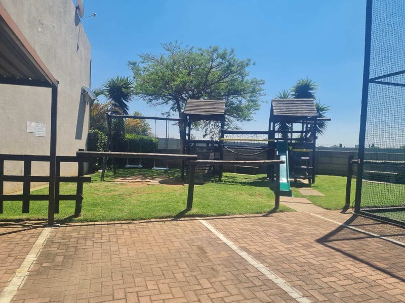 Communal outdoor garden area featuring a paved driveway and a wooden playground structure with swings and a slide.