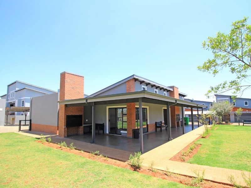 Spacious covered patio featuring a built-in brick braai, overlooking a well-maintained garden area in a modern residential complex.