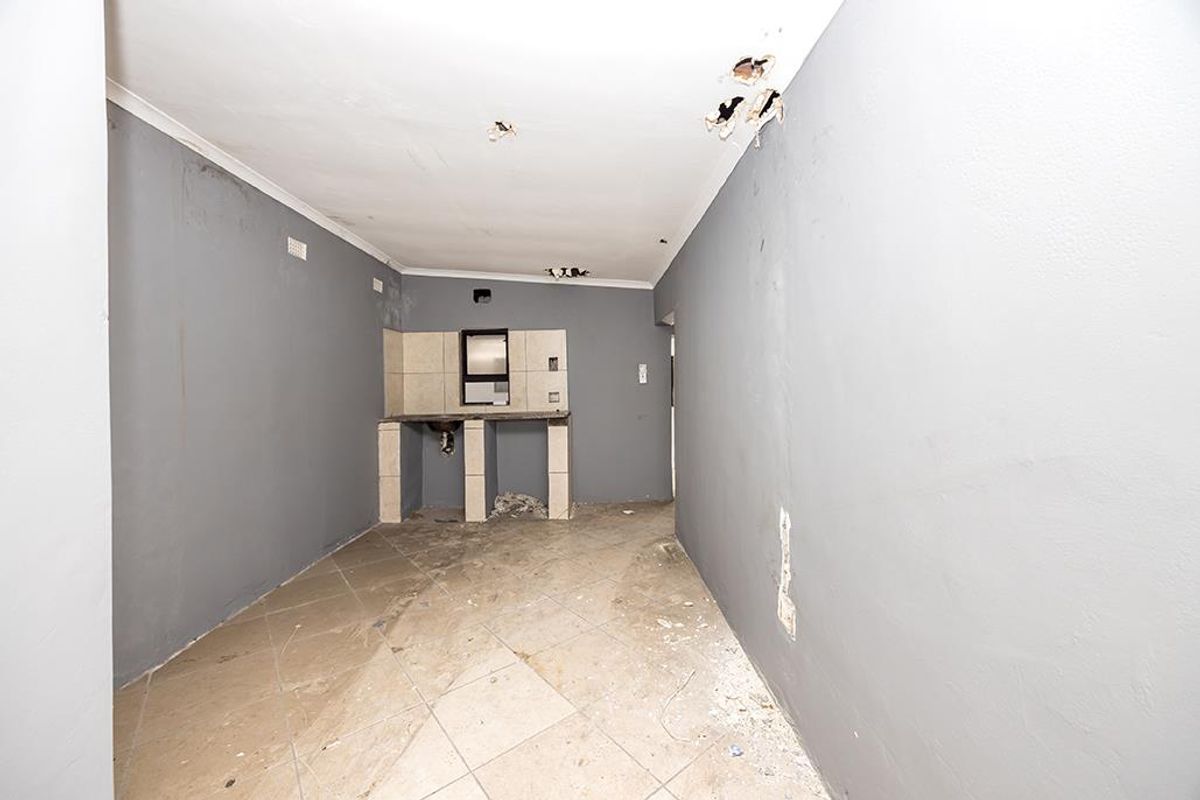 A small, vacant kitchen area featuring tiled flooring, a basic tiled counter, and significant ceiling and wall damage requiring repair.