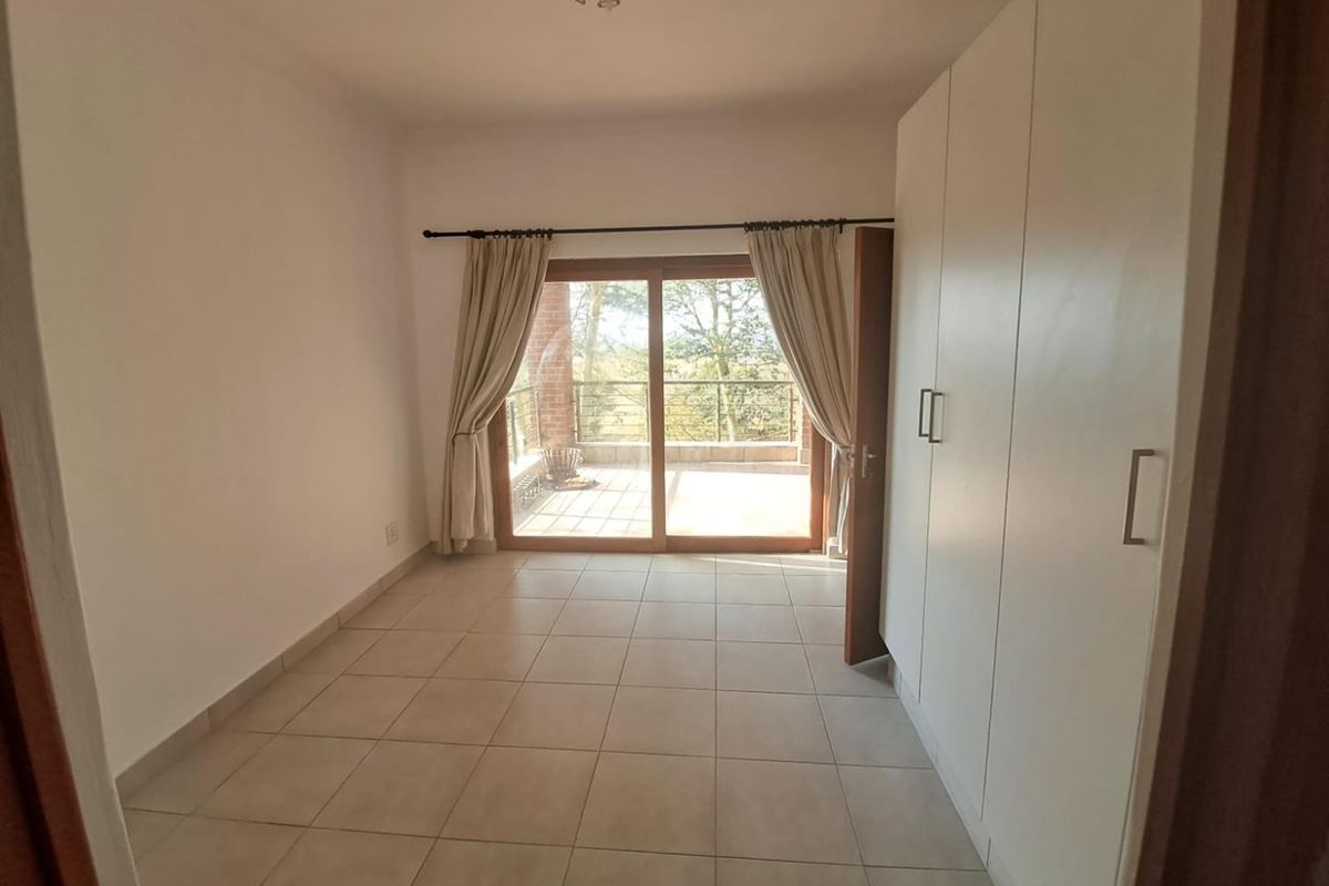 A bright, empty bedroom featuring neutral tiled flooring, built-in white cupboards, and a sliding glass door providing direct access to a private balcony.