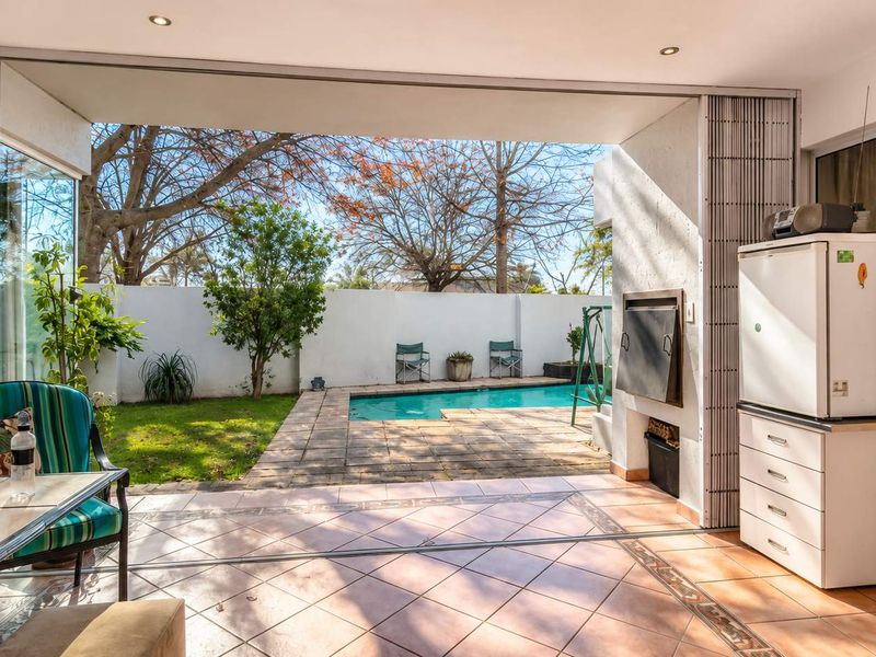 Covered patio area featuring built-in braai, tiled flooring, and seamless flow to the outdoor garden and swimming pool.
