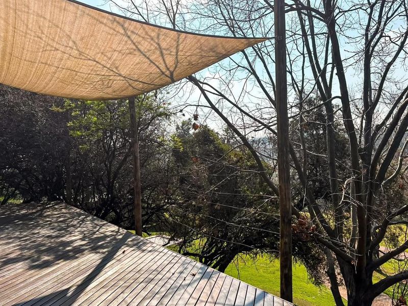An elevated timber deck featuring a shade sail, offering a peaceful outdoor space with views of the surrounding trees and greenery.