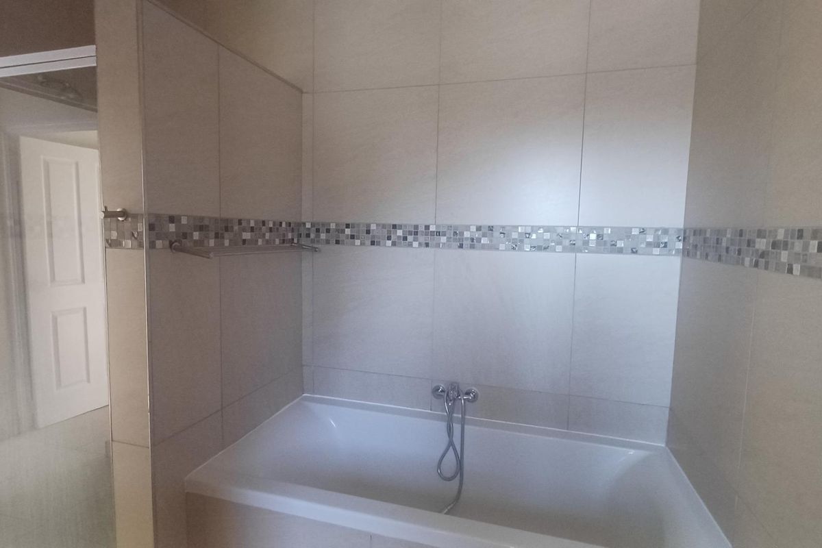 A clean, neutral-toned bathroom featuring a built-in bathtub with chrome fixtures and a separate shower enclosure with tiled wall finishes.