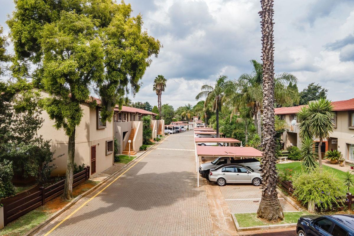 An elevated view of a residential apartment complex featuring paved driveways, covered parking bays, and established landscaping with mature trees.