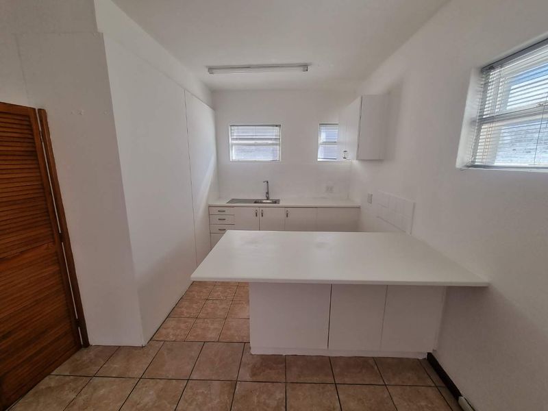 A functional, empty kitchen featuring white built-in cabinetry, a breakfast counter, and tiled flooring, offering a blank canvas for modern updates.