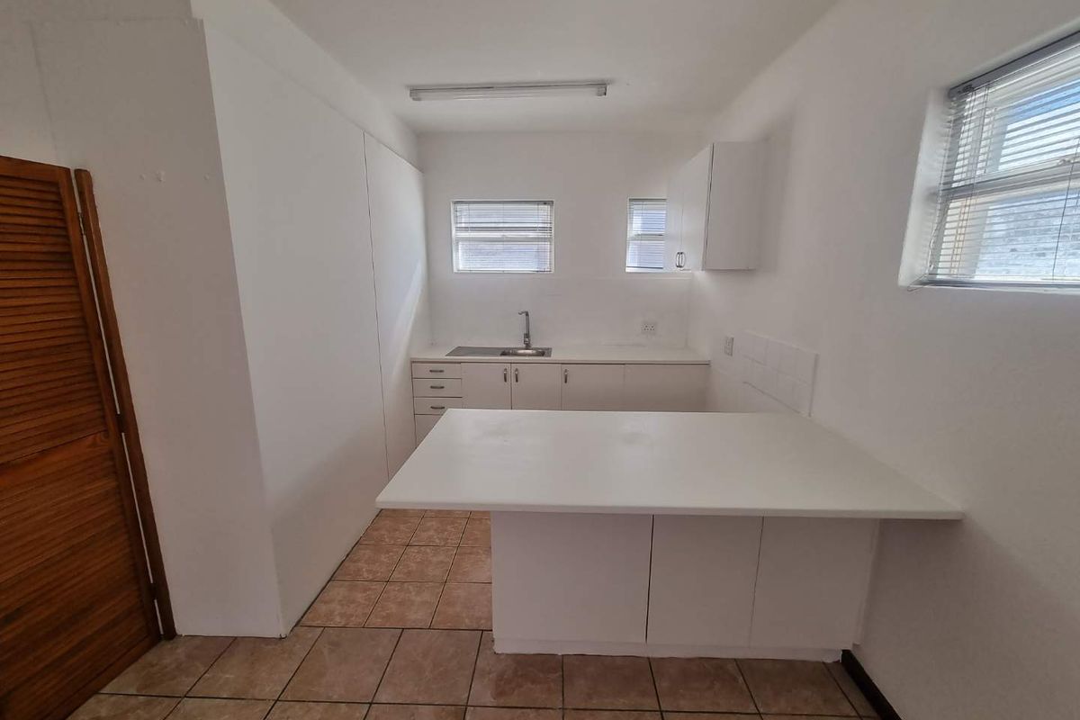 A functional, empty kitchen featuring white built-in cabinetry, a breakfast counter, and tiled flooring, offering a blank canvas for modern updates.