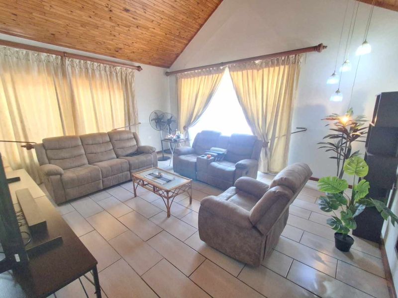 Spacious living room featuring a high vaulted timber ceiling, ceramic tiled flooring, and large windows with natural light.