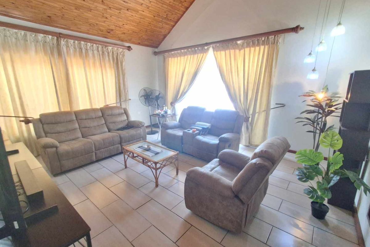 Spacious living room featuring a high vaulted timber ceiling, ceramic tiled flooring, and large windows with natural light.