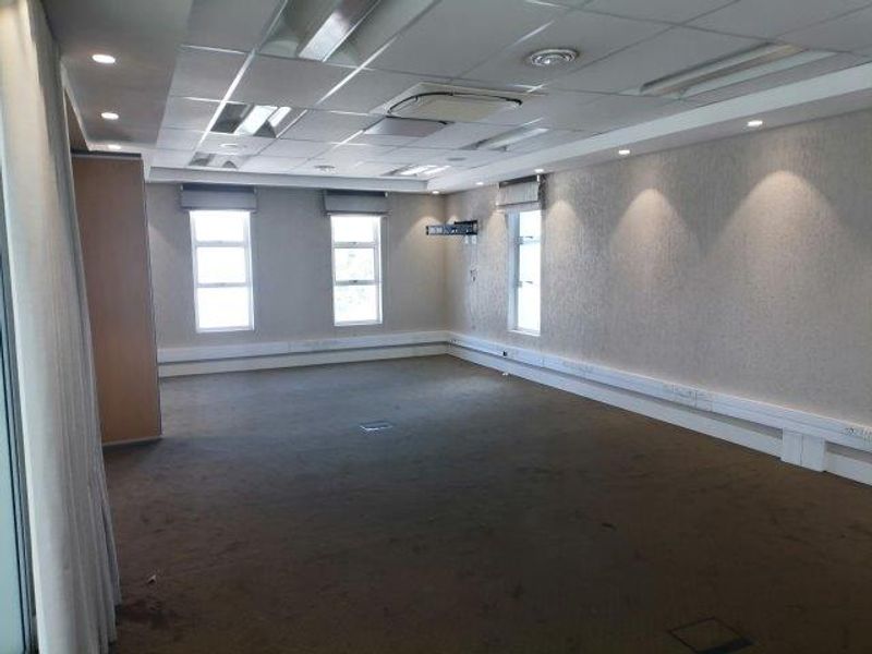 A spacious, empty office area featuring a suspended ceiling with recessed lighting, ducted air conditioning, carpeted flooring, and integrated floor power access points.