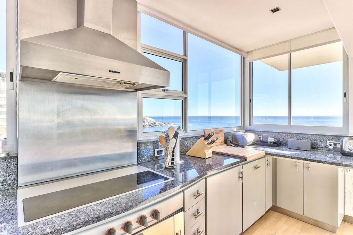 Modern kitchen featuring granite countertops, stainless steel appliances, and expansive windows offering panoramic ocean views.