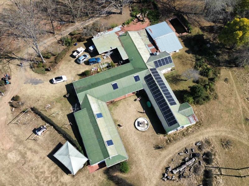 Aerial view of a farm property featuring a large building complex with metal roofing, integrated solar panels, and surrounding rural grounds.