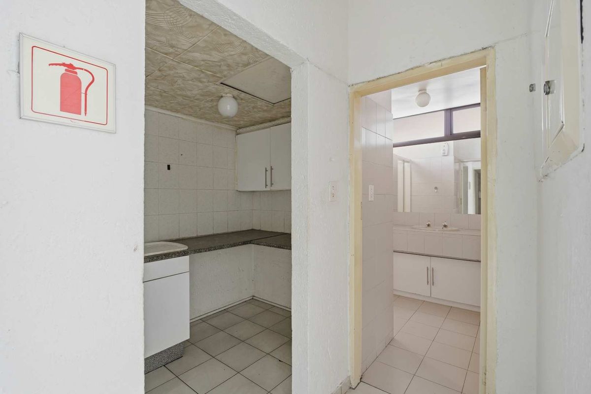 A functional office kitchenette and adjacent bathroom area featuring tiled flooring, built-in cabinetry, and basic utility fixtures.