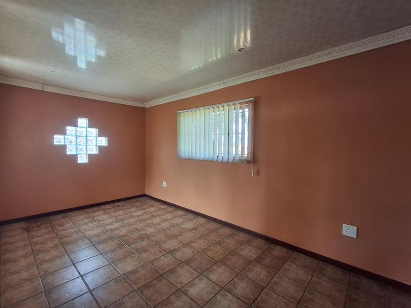 An empty living room featuring terracotta-toned walls, tiled flooring, a decorative glass block window, and a coved ceiling with vertical blinds.
