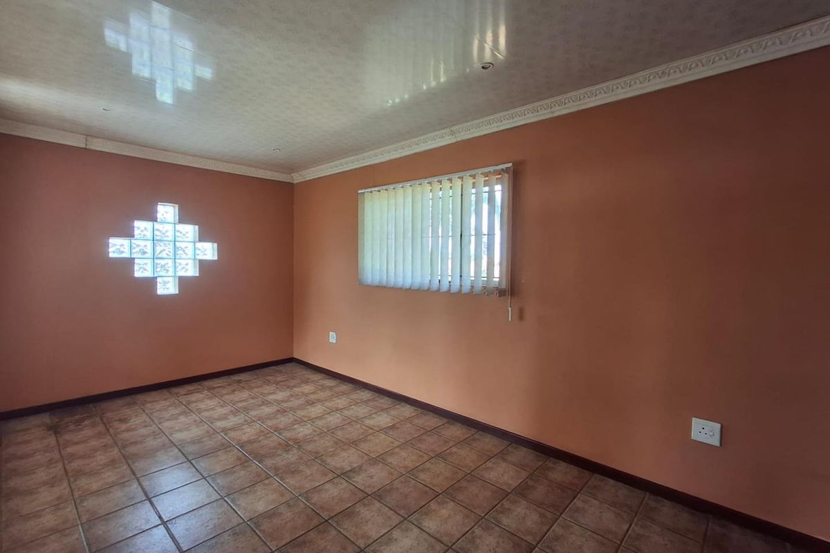 An empty living room featuring terracotta-toned walls, tiled flooring, a decorative glass block window, and a coved ceiling with vertical blinds.