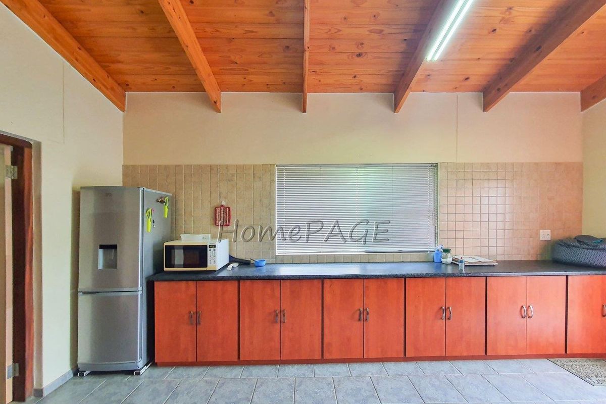 A functional kitchen featuring wooden cabinetry, tiled backsplash, and a high exposed timber beam ceiling with fluorescent lighting.