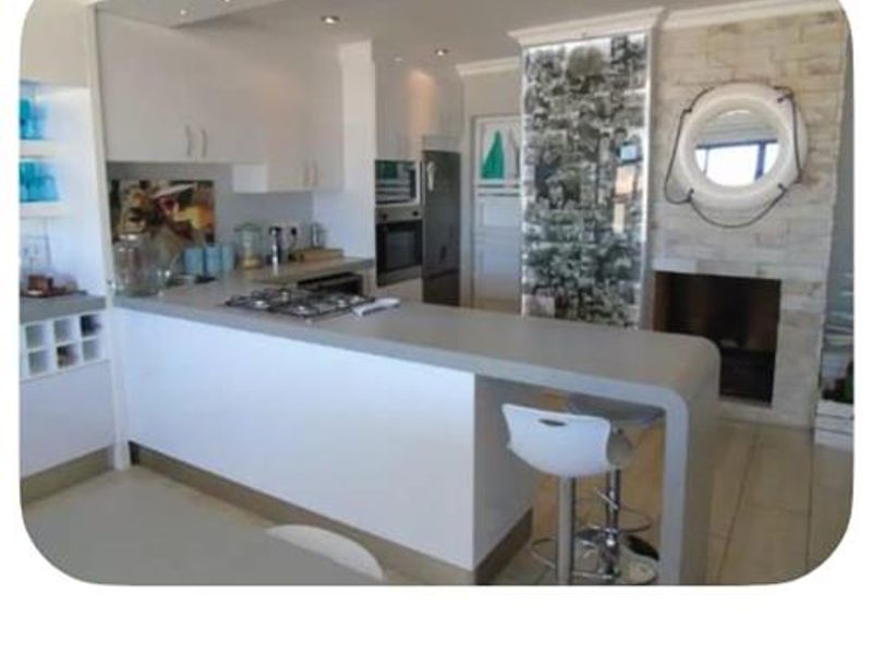 Open-plan kitchen featuring modern white cabinetry, a breakfast bar, and an integrated stone-clad fireplace, creating a cohesive living and cooking space.
