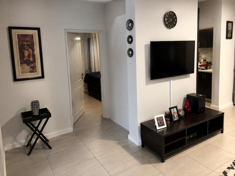 A well-maintained living area featuring neutral tiled flooring, a wall-mounted television, and direct access to an adjacent bedroom.
