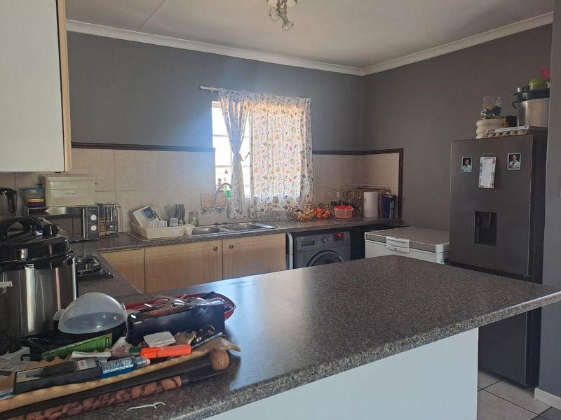 A functional kitchen featuring laminate countertops, built-in cabinetry, a double sink, and a tiled backsplash with space for laundry appliances.