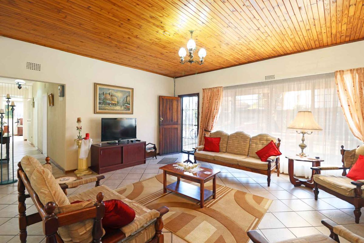 Spacious living room featuring a warm timber tongue and groove ceiling, ceramic tiled flooring, and direct access to the exterior via a security gate.