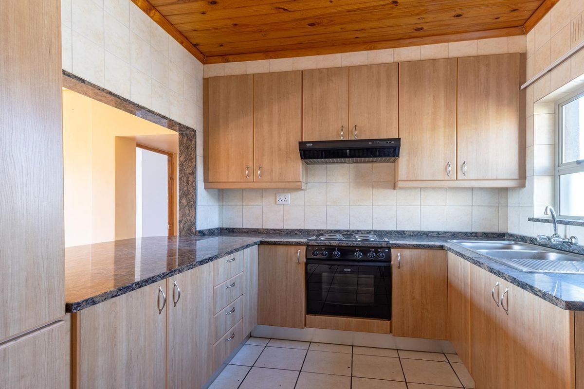 A functional kitchen featuring light wood cabinetry, granite countertops, a built-in oven with extractor fan, and tiled flooring.