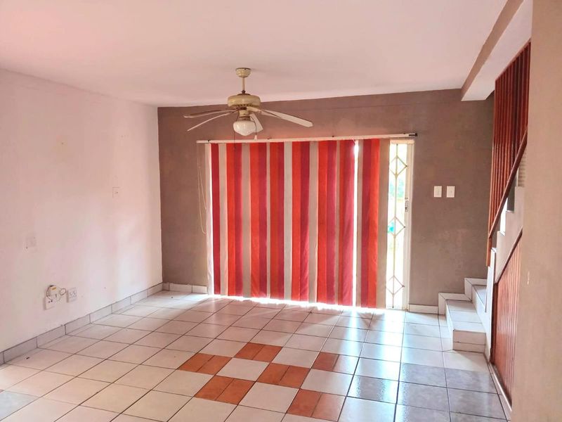 An empty living room featuring tiled flooring, a ceiling fan, and a staircase with a wooden balustrade, leading to an exterior security gate.
