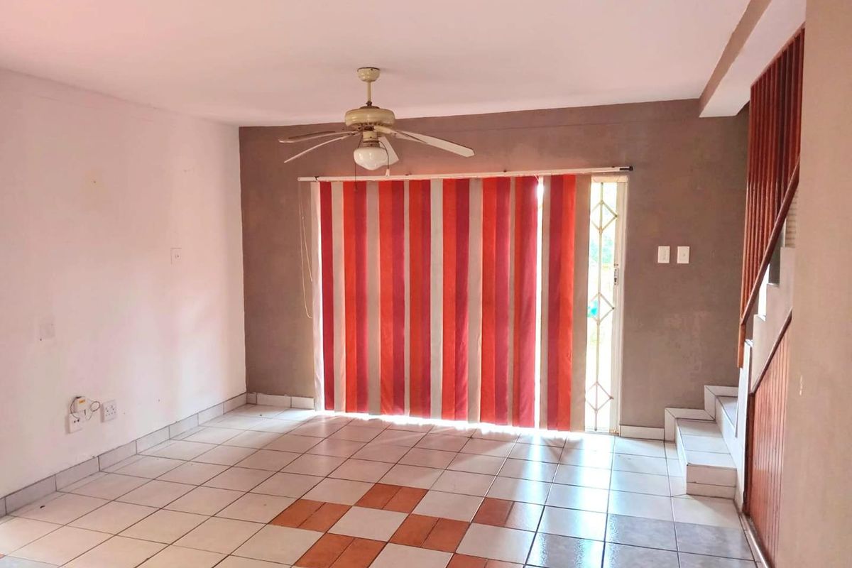 An empty living room featuring tiled flooring, a ceiling fan, and a staircase with a wooden balustrade, leading to an exterior security gate.