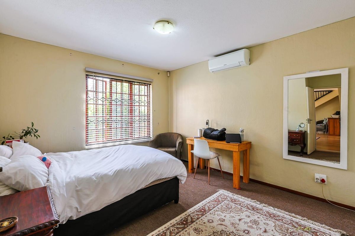 A bedroom featuring a wall-mounted air conditioning unit, security bars on the window, and carpeted flooring.