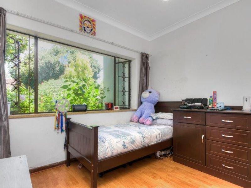 A bedroom featuring laminate flooring, a large window with security bars, and cove cornicing, offering a functional space with natural light.