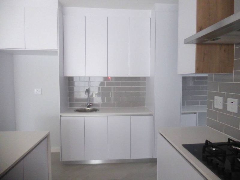 Modern kitchen featuring clean white cabinetry, grey subway tile backsplash, stone countertops, and integrated gas hob with extractor fan.