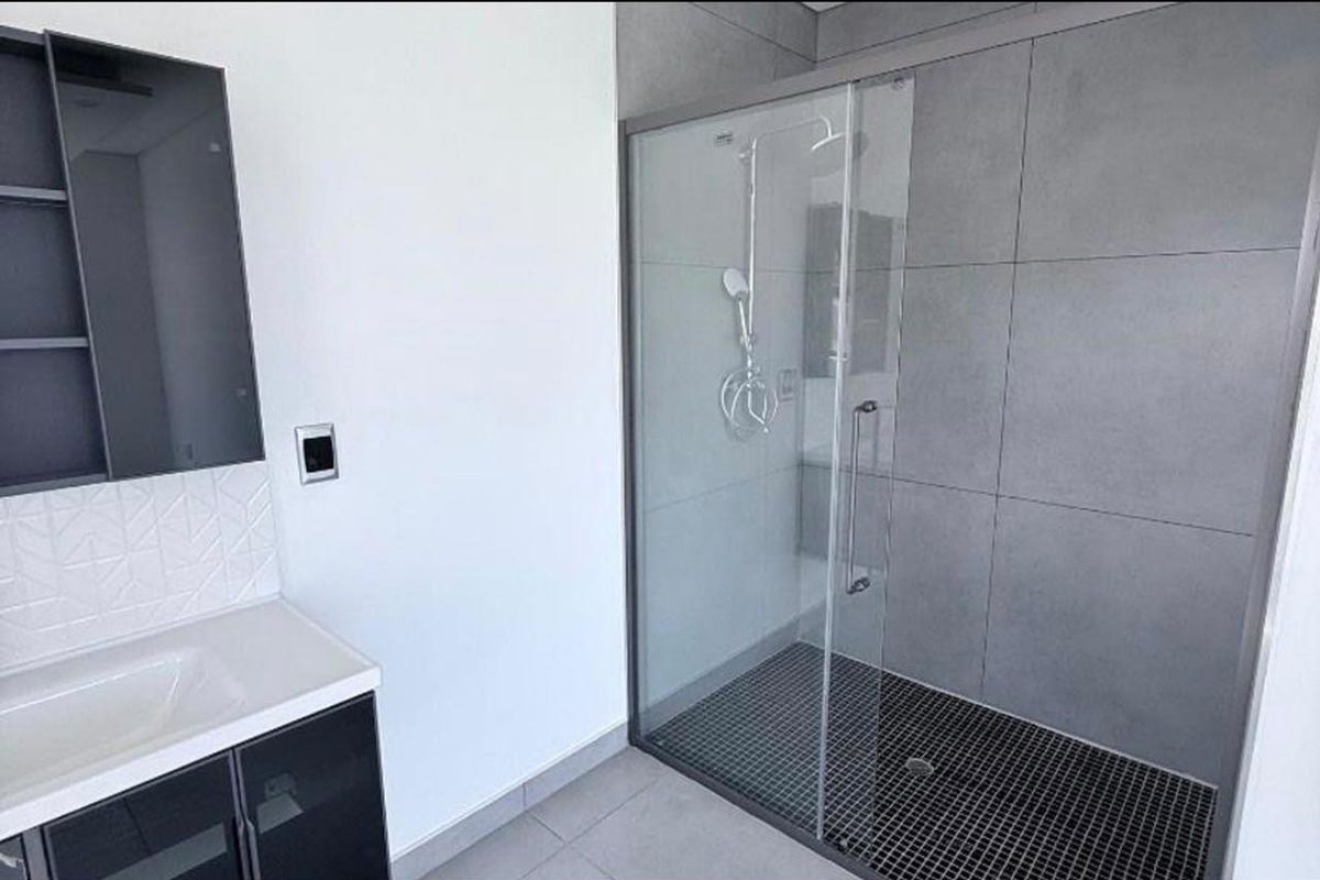 Modern bathroom featuring a spacious walk-in shower with glass enclosure, contemporary vanity cabinet, and sleek grey tiling throughout.
