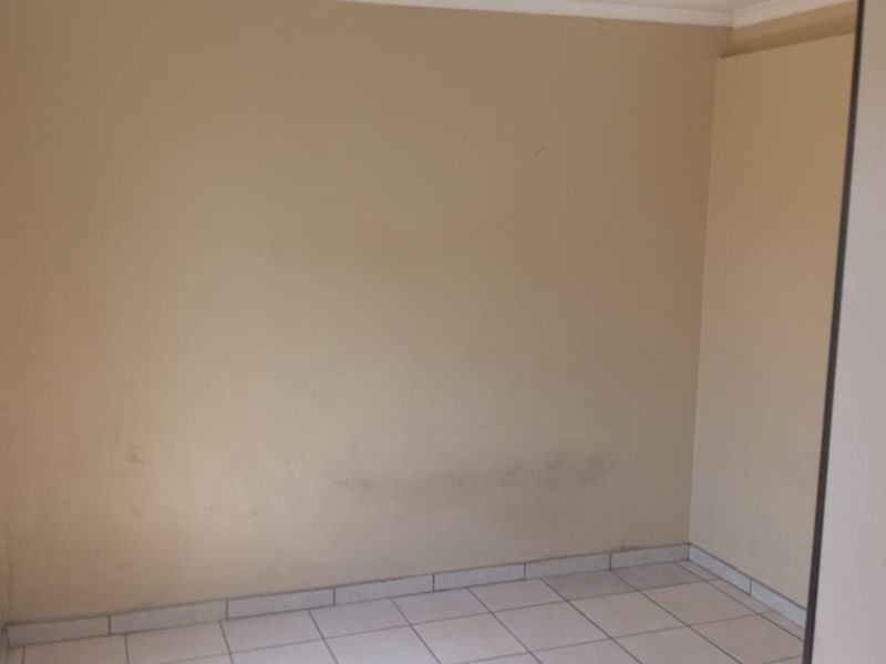 An empty bedroom featuring tiled flooring and neutral wall finishes, requiring minor cosmetic attention to address surface marks on the walls.