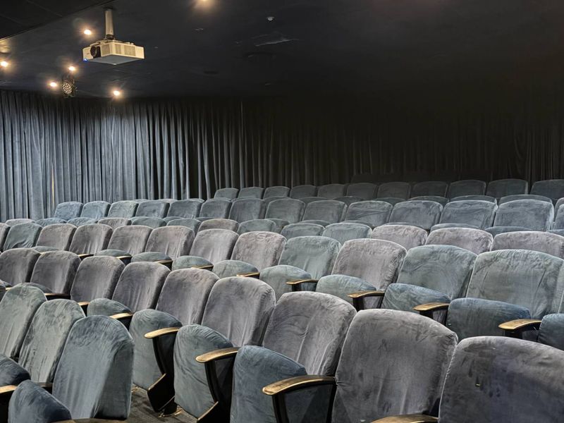 A dedicated cinema room featuring tiered theatre-style seating, acoustic wall curtains, and a ceiling-mounted projector for an immersive viewing experience.