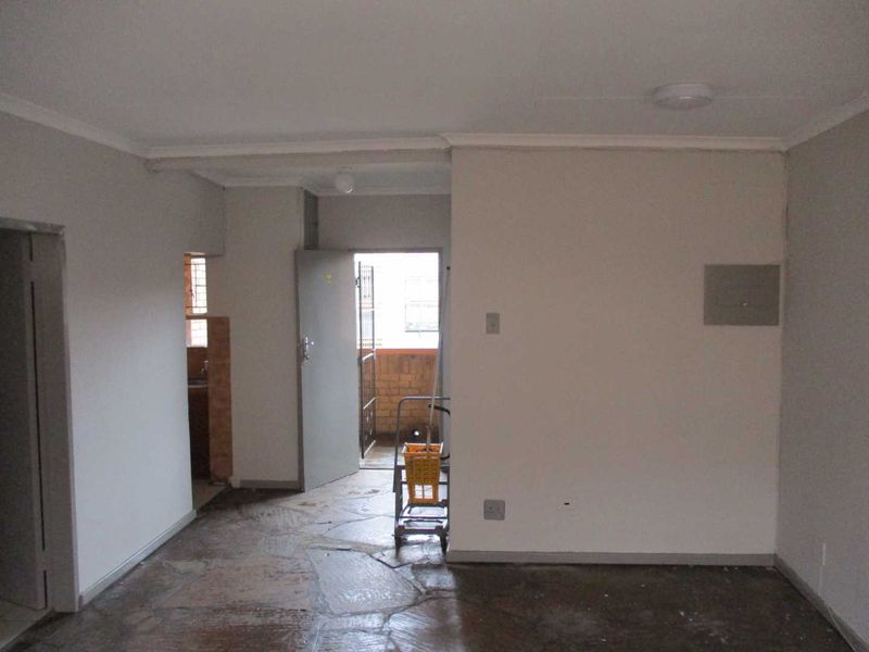 An empty living area featuring stone flooring, neutral walls, and access to an exterior balcony through a security gate.