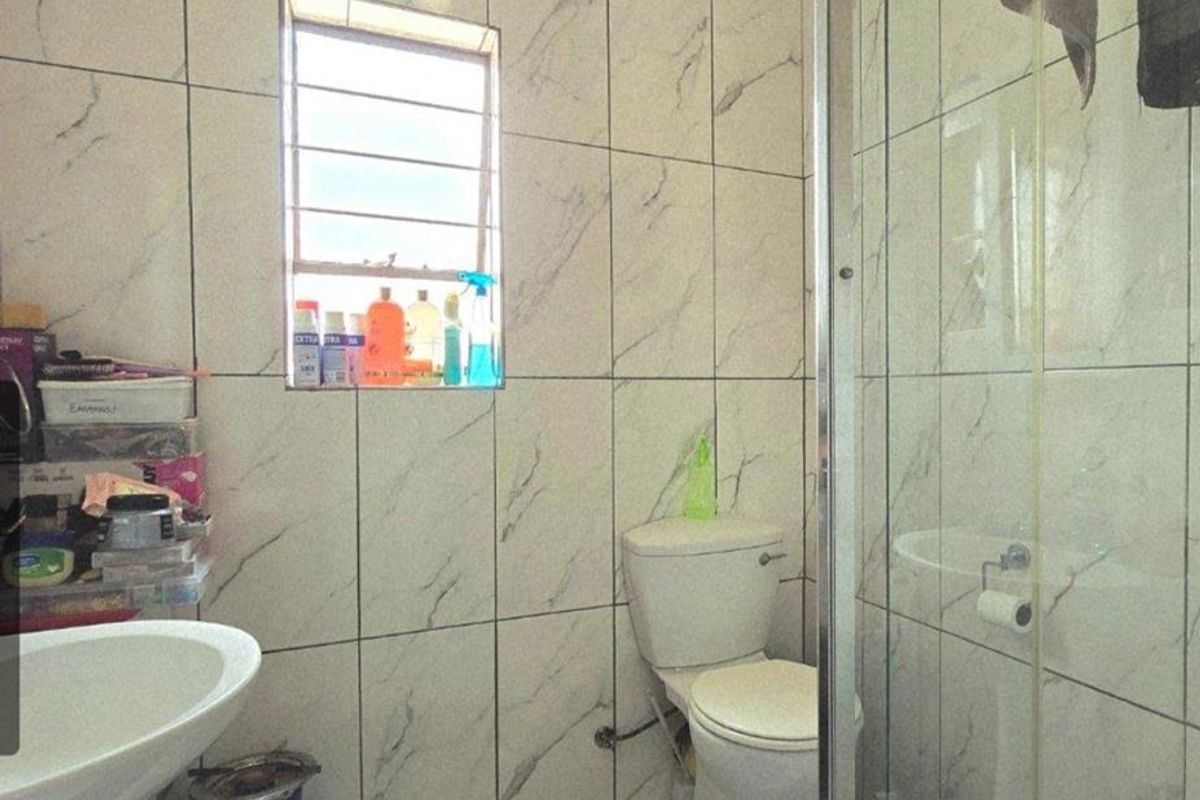 A compact bathroom featuring marble-look wall and floor tiles, a pedestal basin, a standard toilet, and a glass-enclosed shower cubicle.