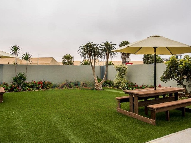 A well-maintained outdoor garden area featuring artificial turf, perimeter walling, and paved pathways, providing a clean and functional space for guests.