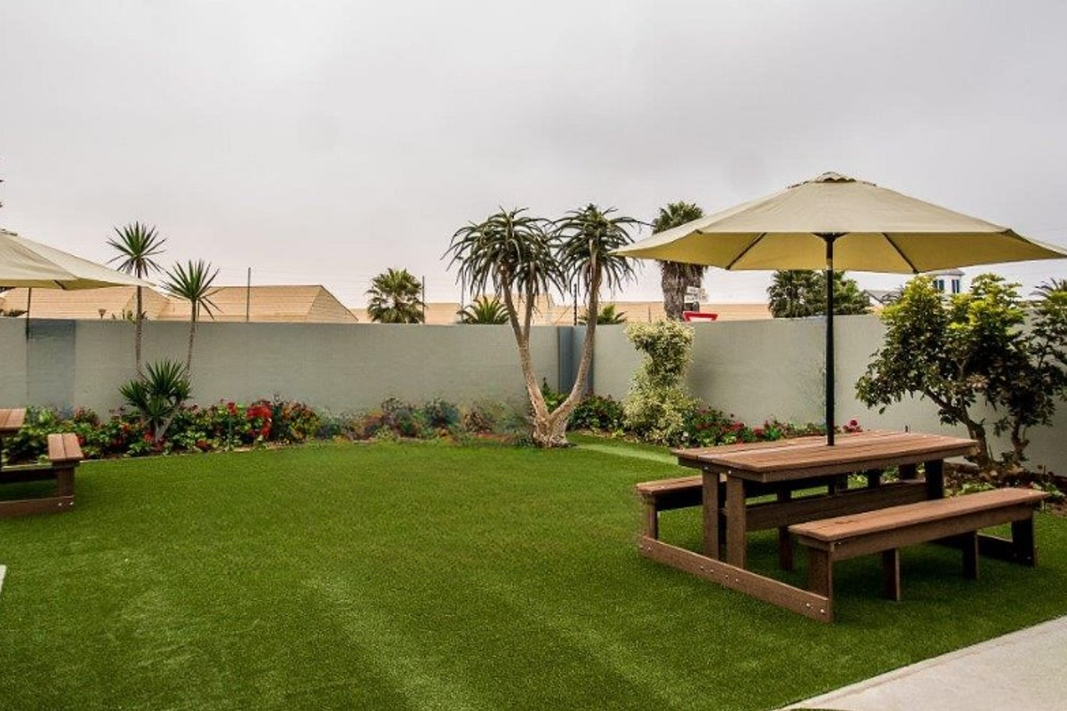 A well-maintained outdoor garden area featuring artificial turf, perimeter walling, and paved pathways, providing a clean and functional space for guests.