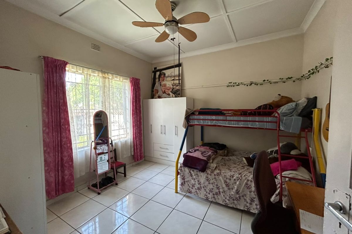 A functional bedroom featuring tiled flooring, a ceiling fan, and a built-in wardrobe with security bars installed on the window.