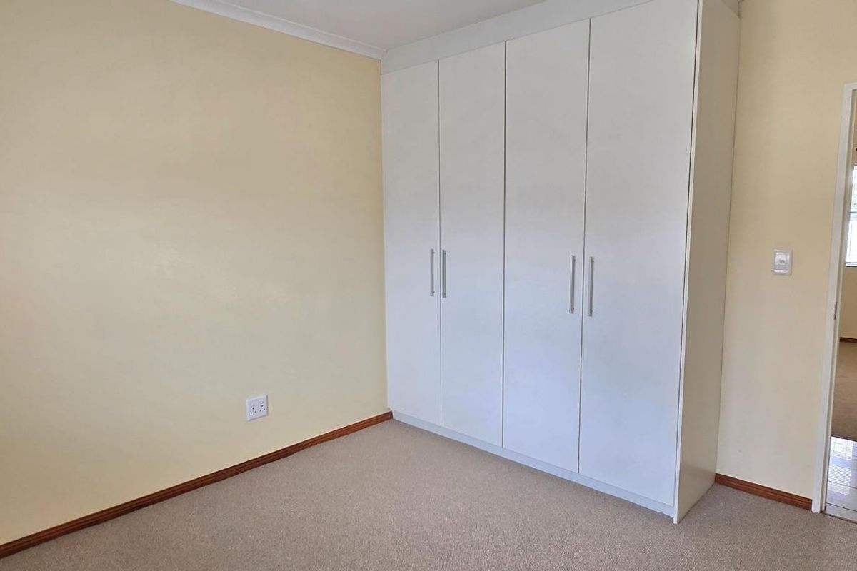 A clean, empty bedroom featuring neutral walls, fitted carpet flooring, and built-in white cabinetry, with a doorway leading to an adjacent room.