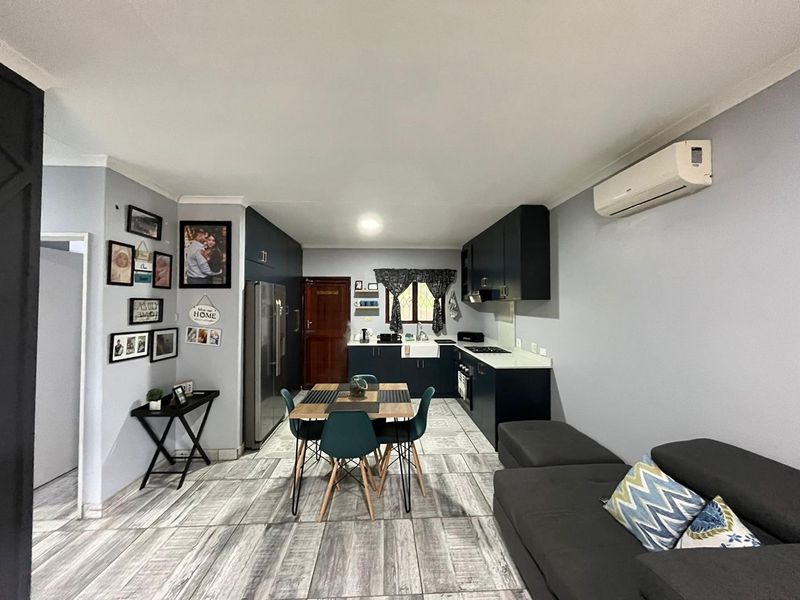 Open-plan living and kitchen area featuring dark cabinetry, modern tiled flooring, and a wall-mounted air conditioning unit.