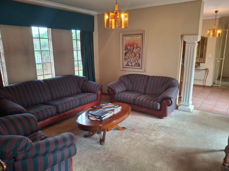 A spacious living room featuring carpeted flooring, a decorative column, and access to an adjacent tiled area, offering a comfortable and traditional layout.