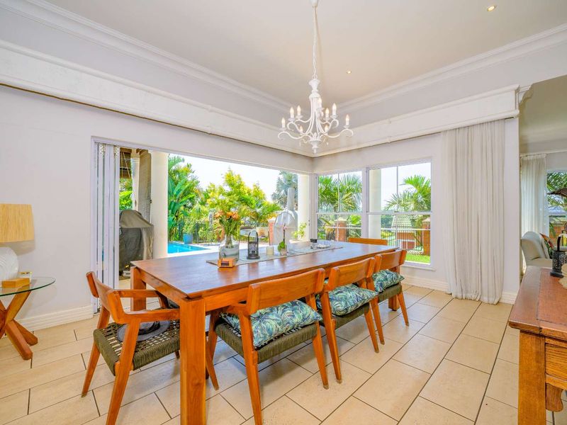 Bright dining room featuring tiled flooring, crown molding, and large stacking glass doors that open to an outdoor patio and pool area.