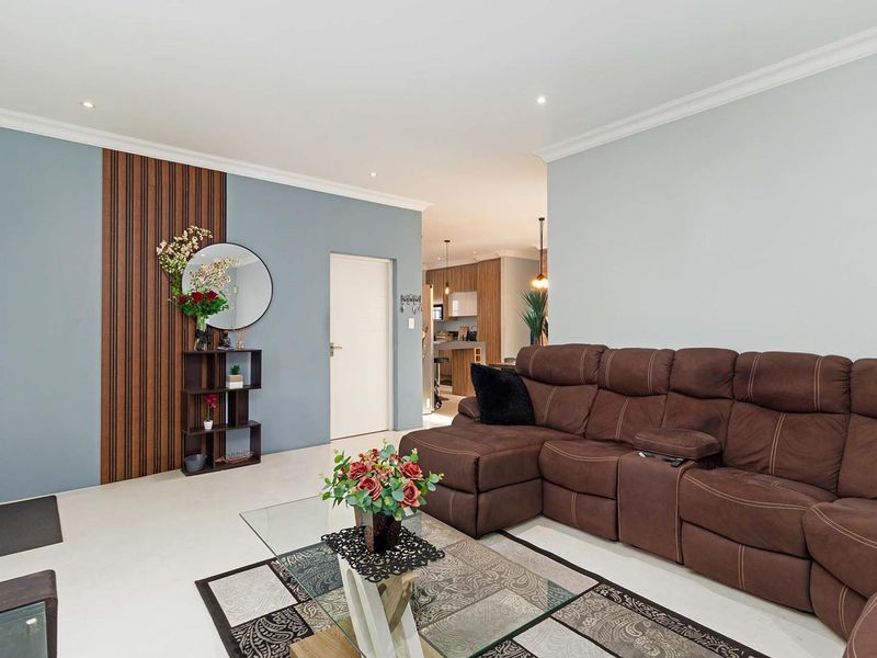 Open plan living area featuring tiled floors, recessed downlights, and a decorative timber feature wall, with a view through to the kitchen area.