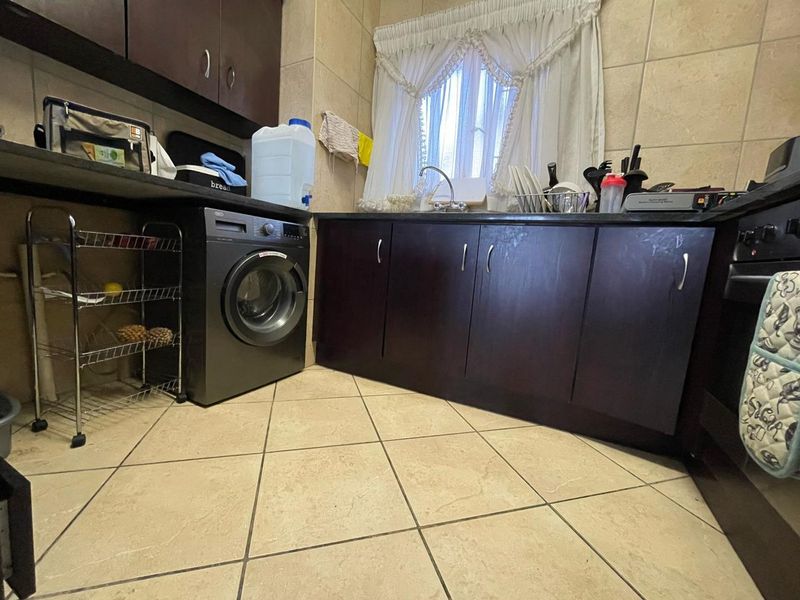 A functional kitchen featuring dark wood cabinetry, stone countertops, tiled flooring, and a built-in oven with integrated laundry plumbing.